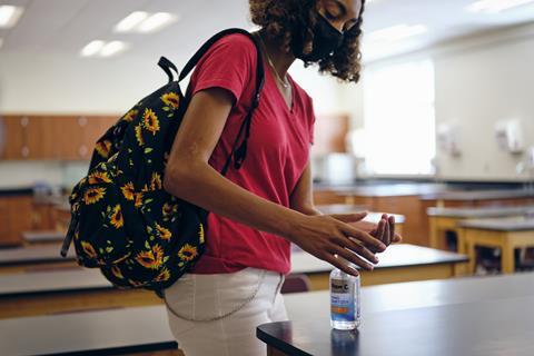 A photo of a highschool student in a face mask using hand sanitizer