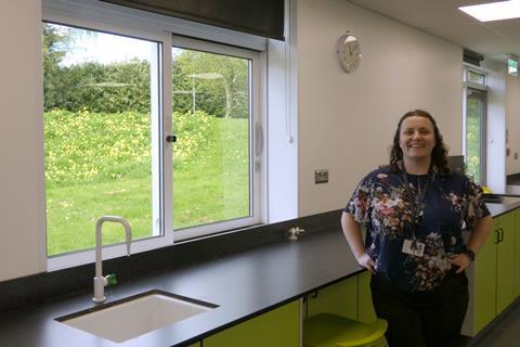 A teacher in a modern science classroom looking out of a window at a wildflower meadow