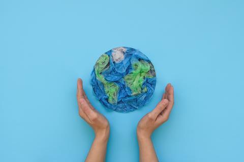 Two hands on either side of a circle of green and blue disposable plastic resembling the Earth