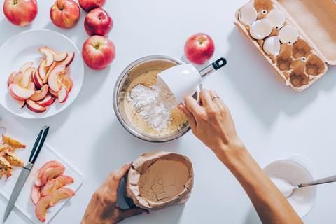 A photo from above of someone adding a cup of flour to a mixing bowl