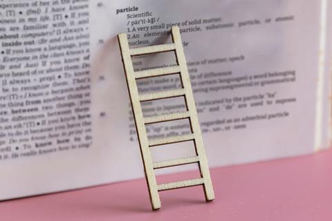 A small ladder leans on a book showing the definition of the word particle