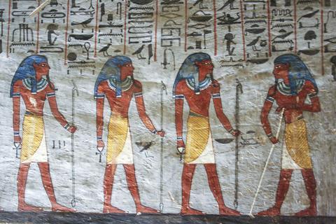 An ancient Egyptian painting on a wall showing hieroglyphics and four standing figures with blue hair