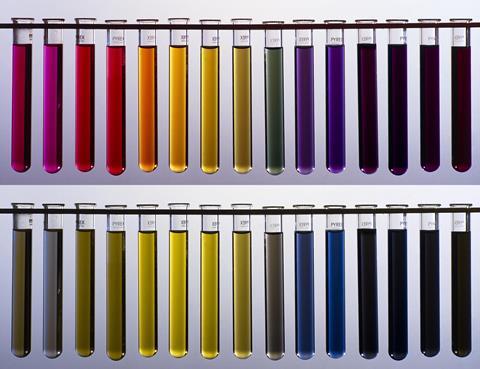 Two rows of test tubes containing liquids of different colours. The top shows a rainbow range from red through to dark purple and the bottom shows a muted range of dark greens and blues