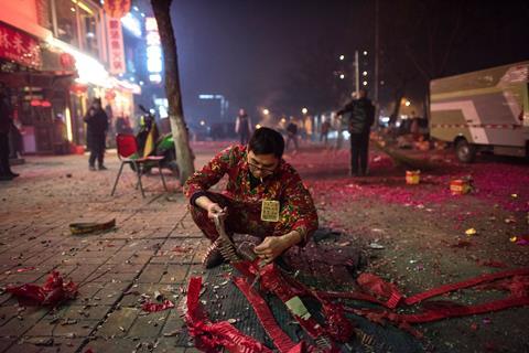 An image showing a waiter from a restaurant lighting fireworks on a street in Beijing on February 7, 2016, the eve of the Lunar New Year. 
