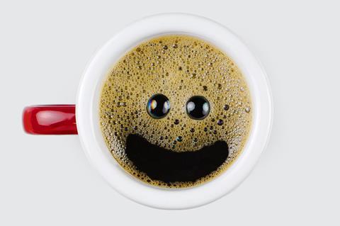 A photo of a cup of coffee with a smiley face appearing in the bubbles