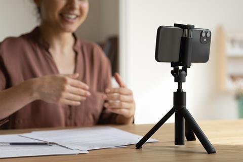 A woman recording herself explaining something on a mobile phone that's sitting on a tripod