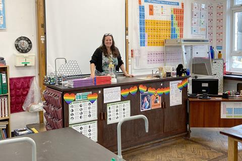 An image of Jennifer Pierce stood at her desk with a periodic table and other chemistry decorations.