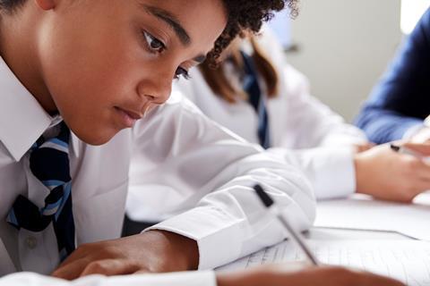 A photograph of a male student in school uniform working individually at a desk