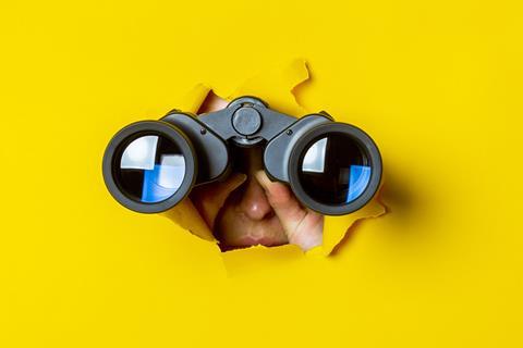 Someone with a pair of binoculars bursting through a wall of yellow paper