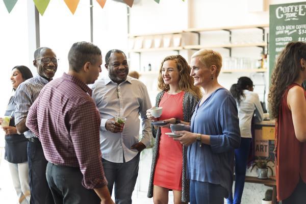 A diverse group of people stand talking and smiling at an event