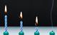 An image showing four stripey blue and white candles, all alight, from left to right, they show the progression of burning