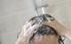 A photograph of a woman washing her hair in the shower; the woman is using her hands to apply shampoo