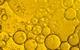 A close-up photograph showing circles of yellow-gold cooking oil floating on water