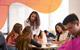 A female teacher talks with a group of students at a table in their classroom, while two of the students make notes