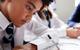 A photograph of a male student in school uniform working individually at a desk