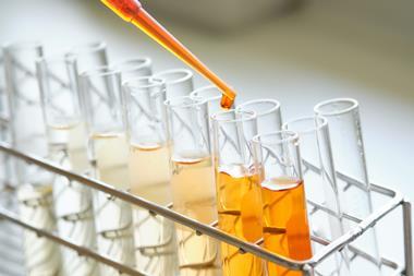 A photograph of a pipette held above test tubes in a metal test tube rack, containing different concentrations of an orange solution