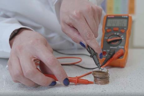 A female scientist applies a voltmeter to a coin battery on a work bench, to test how different electrolytes perform