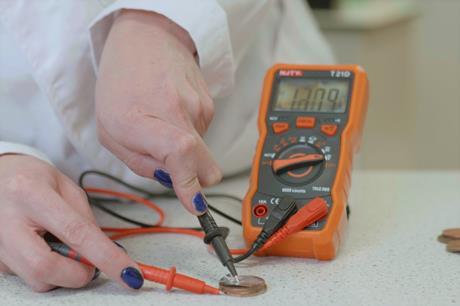 A scientist applies a voltmeter to a coin battery on a work bench, to test how different electrolytes perform