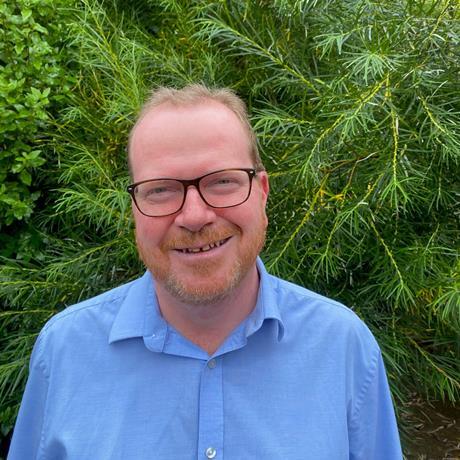 Tim Jolliff stands and smiles with foliage in the background