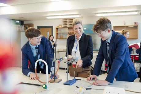 A photograph of two secondary school students and their teacher smiling while discussing an experiment in a chemistry lesson