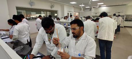 Chemistry teachers wearing lab coats and safety goggles conduct experiments in a laboratory during a teacher training session